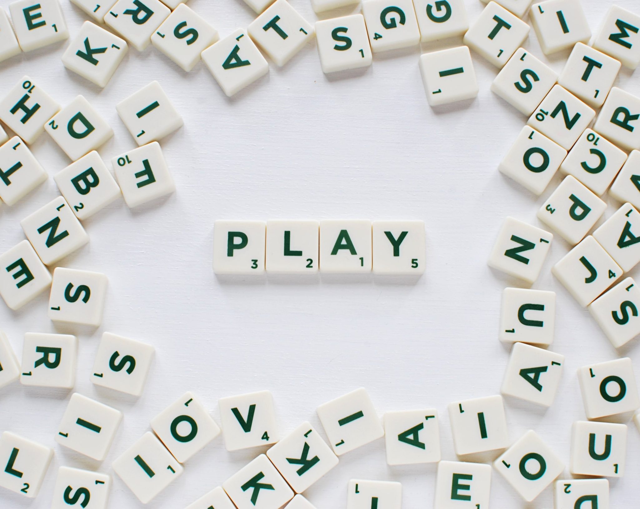 Scrabble pieces all over white table spelling out PLAY